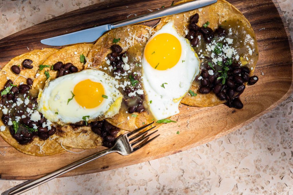 sunny side up eggs over tortillas with black beans and salsa verde