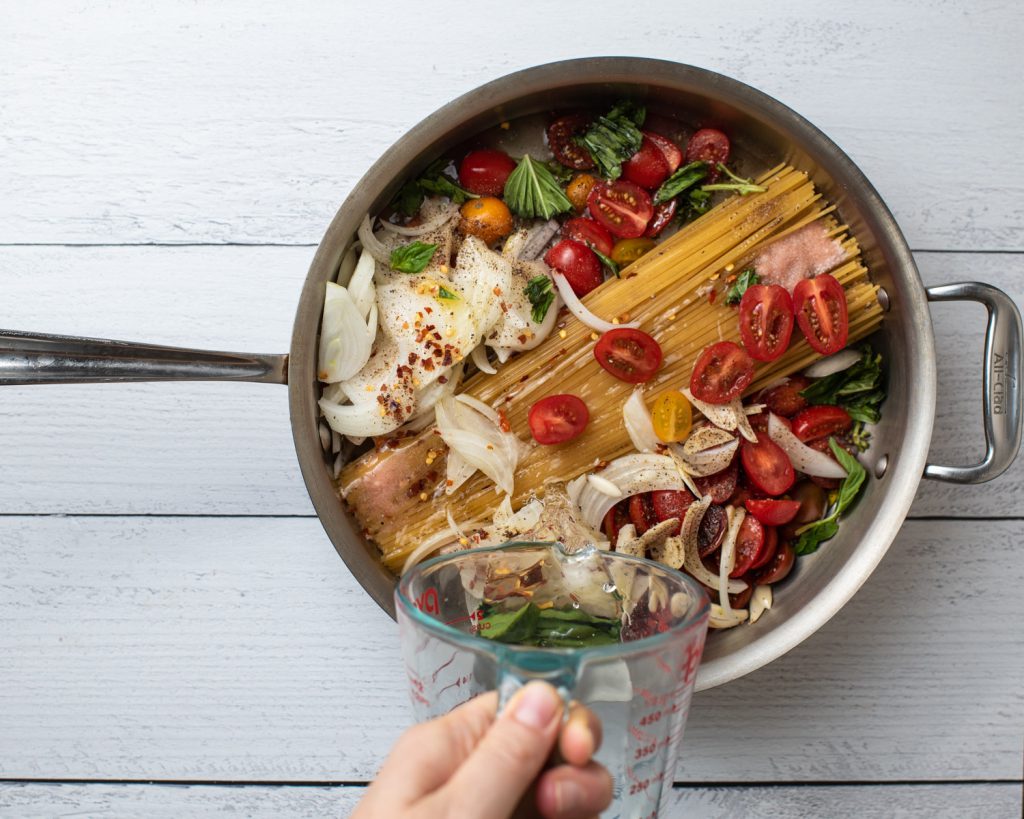 saute pan with spaghetti noodles onion tomato and basil